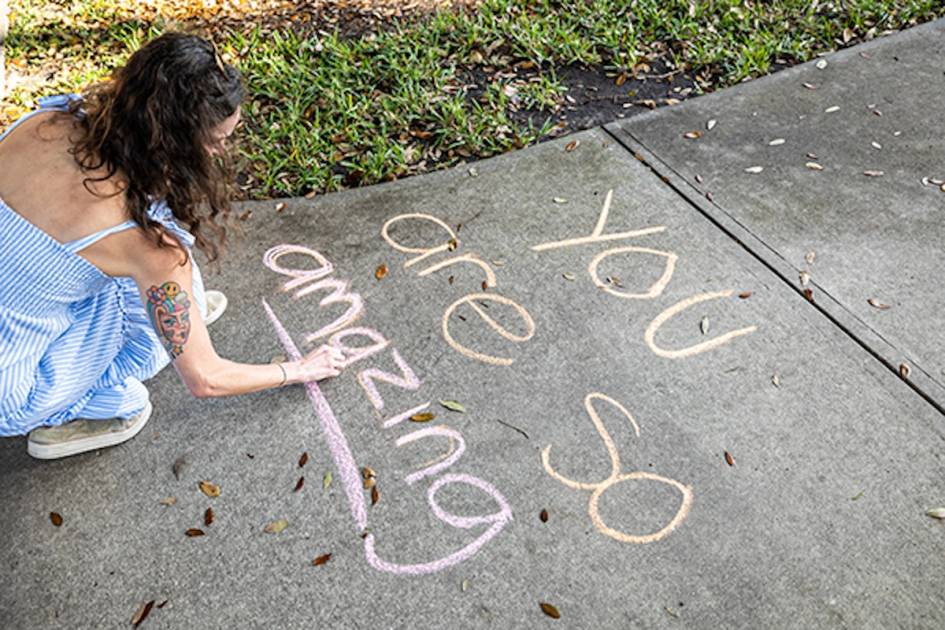 Student writing "You are so amazing" on sidewalk with chalk