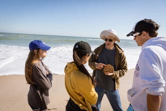 A Rollins professor discusses a piece of coral with students on the beach.