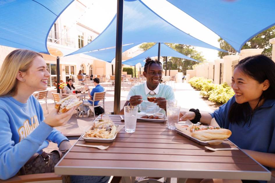 Three students share lunch together on an outdoor patio.