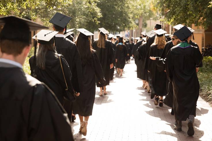 College graduates walk toward a commencement ceremony in caps and gowns.