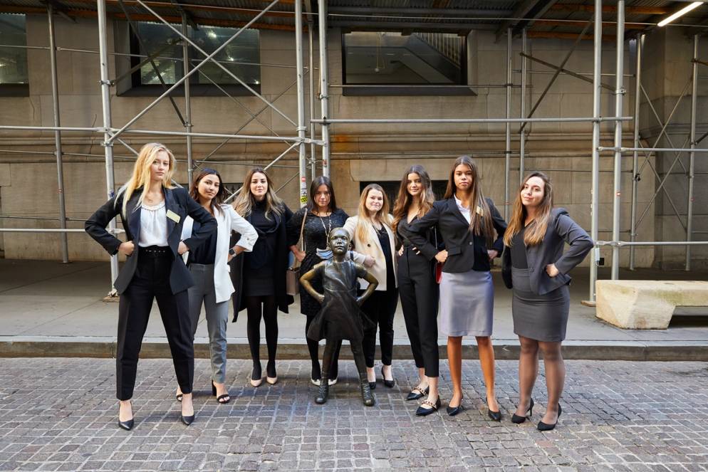 Women in Finance students pose with the iconic Fearless Girl statue on Broad Street across from the New York Stock Exchange in the Financial District of Manhattan.