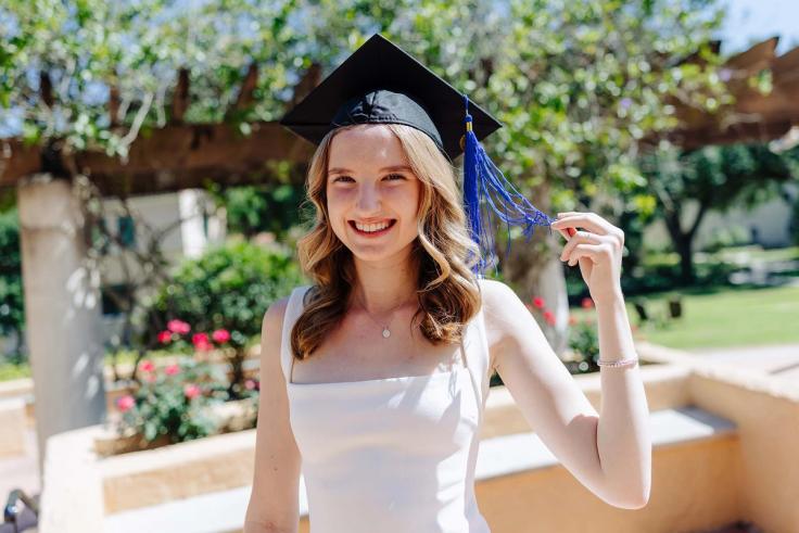 Kate Salerno poses outdoors in a white dress and graduation cap with a blue tassel. 