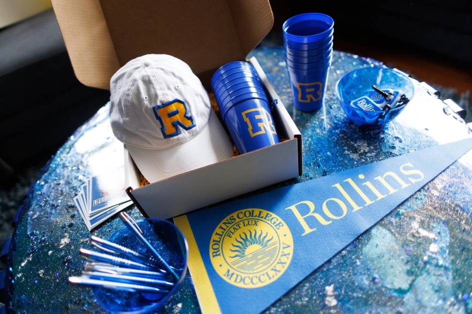 An open box with Rollins hat, cups, pendant, pens and stickers.