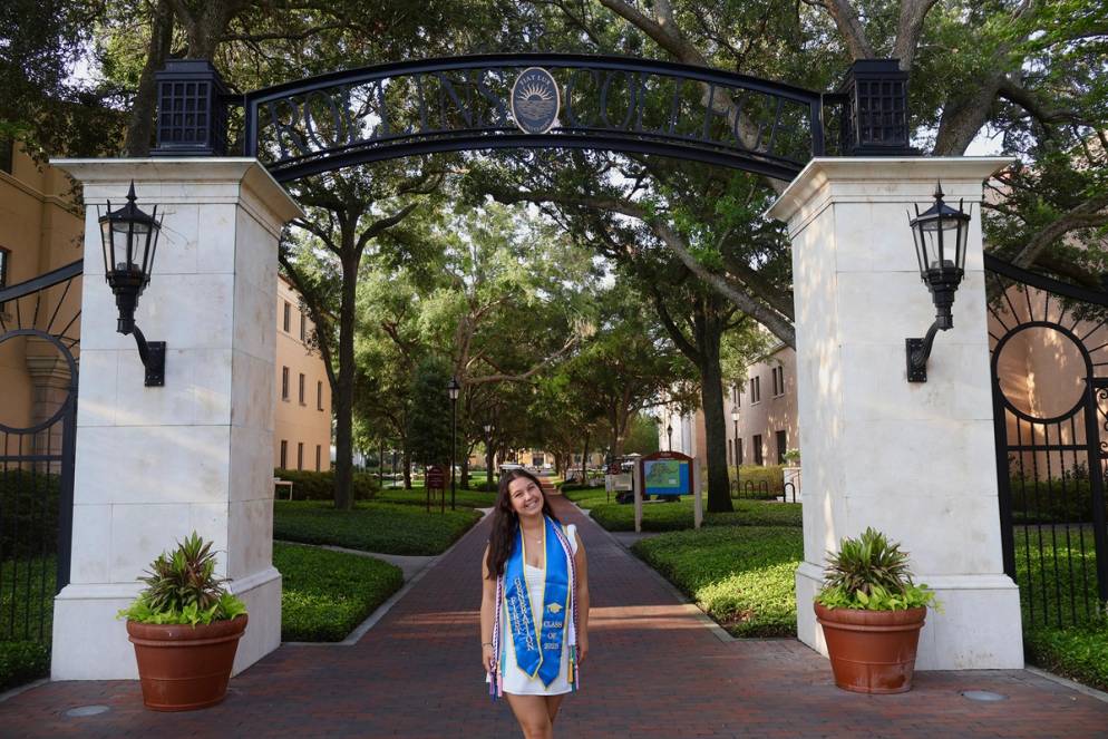 Sophia Cassa in front of the Rollins archway in graduation regalia