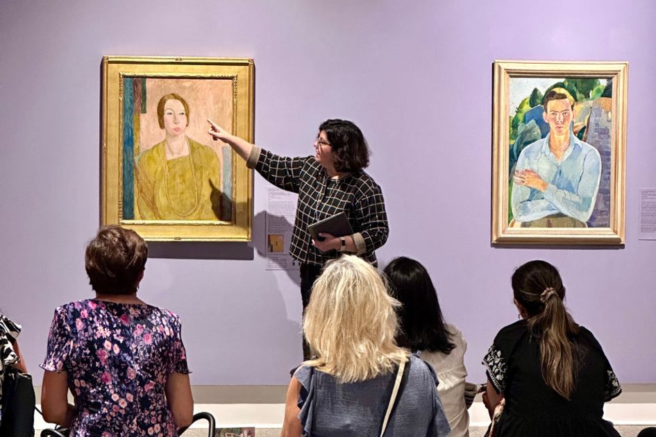 Museum guide explaining portrait painting to seated visitors in gallery