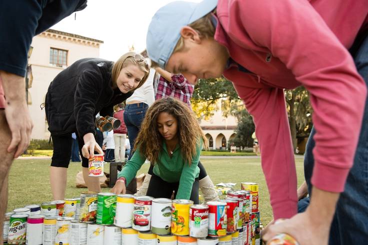 Three college students stack cans of food during a campus food drive.