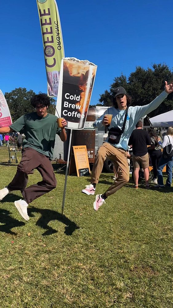People jumping excitedly with iced coffees at an outdoor cold brew stand