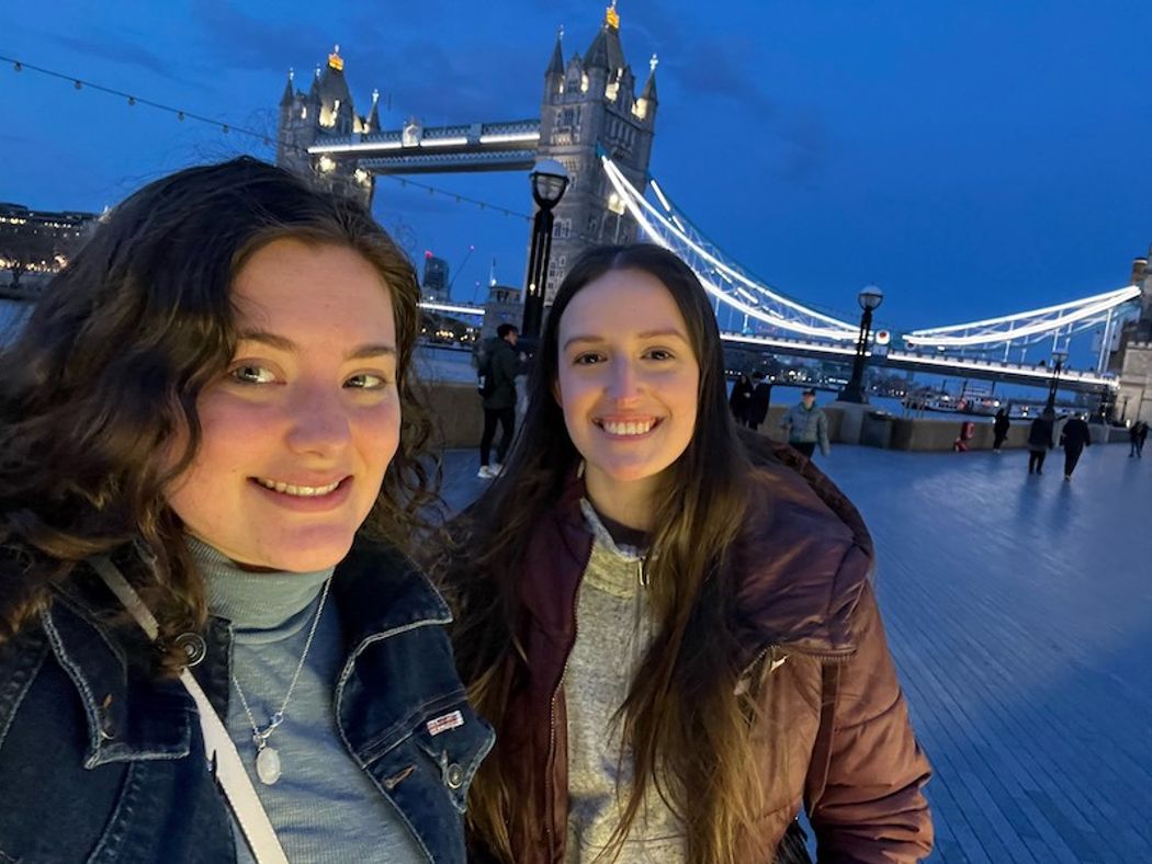 Students smiling to camera with the London Bridge at night behind them.