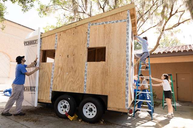 Liberal arts college students wrapping a tiny home with water proofing.