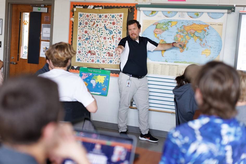 A middle school teacher points to a student while leading a classroom discussion.