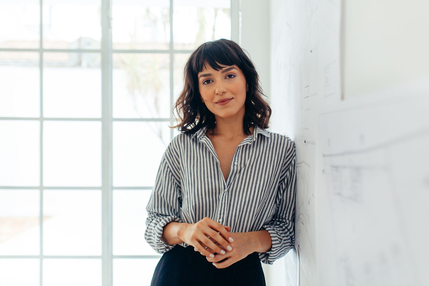 A businesswoman leans against a white board.