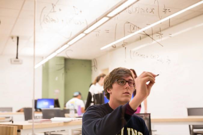 Student working out a math equation on a glass wall.