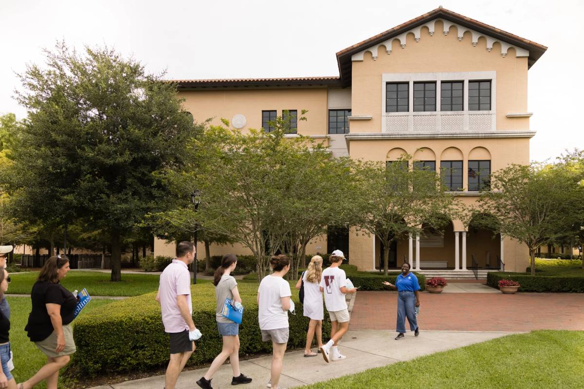 Campus tour group walking past academic building with guide leading discussion.