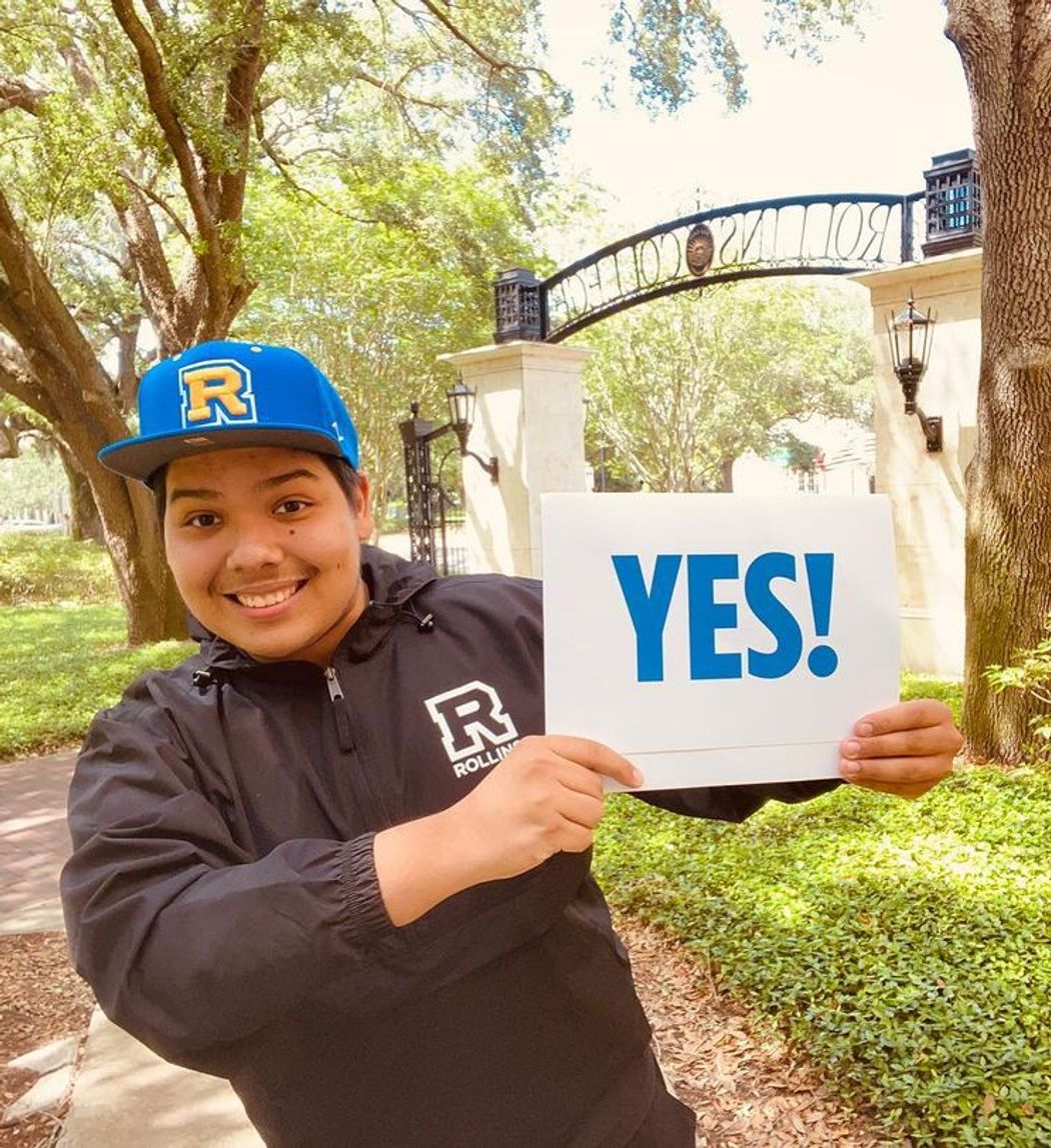 Student excited to be attending Rollins, wearing school gear and holding an acceptance letter.