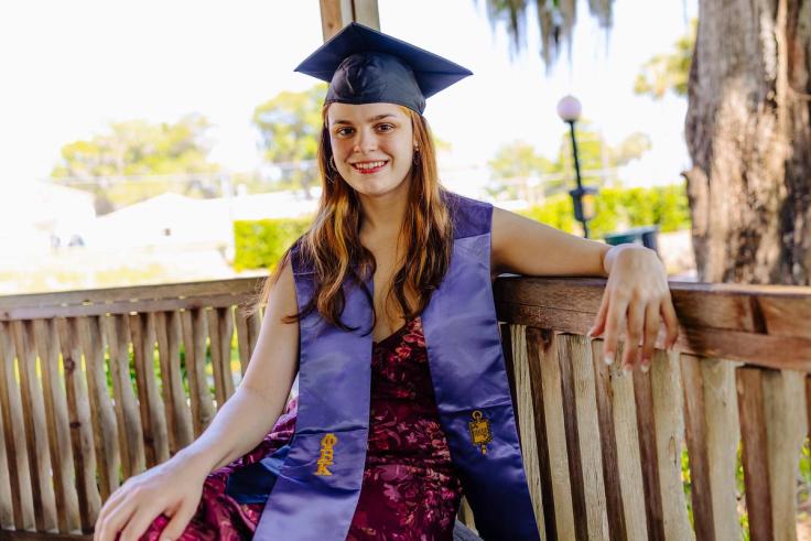 Lindsey Scanlan sits in a gazebo while wearing graduation regalia.