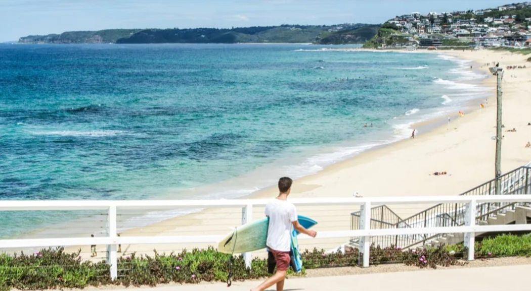 Student with surfboard heading to beach