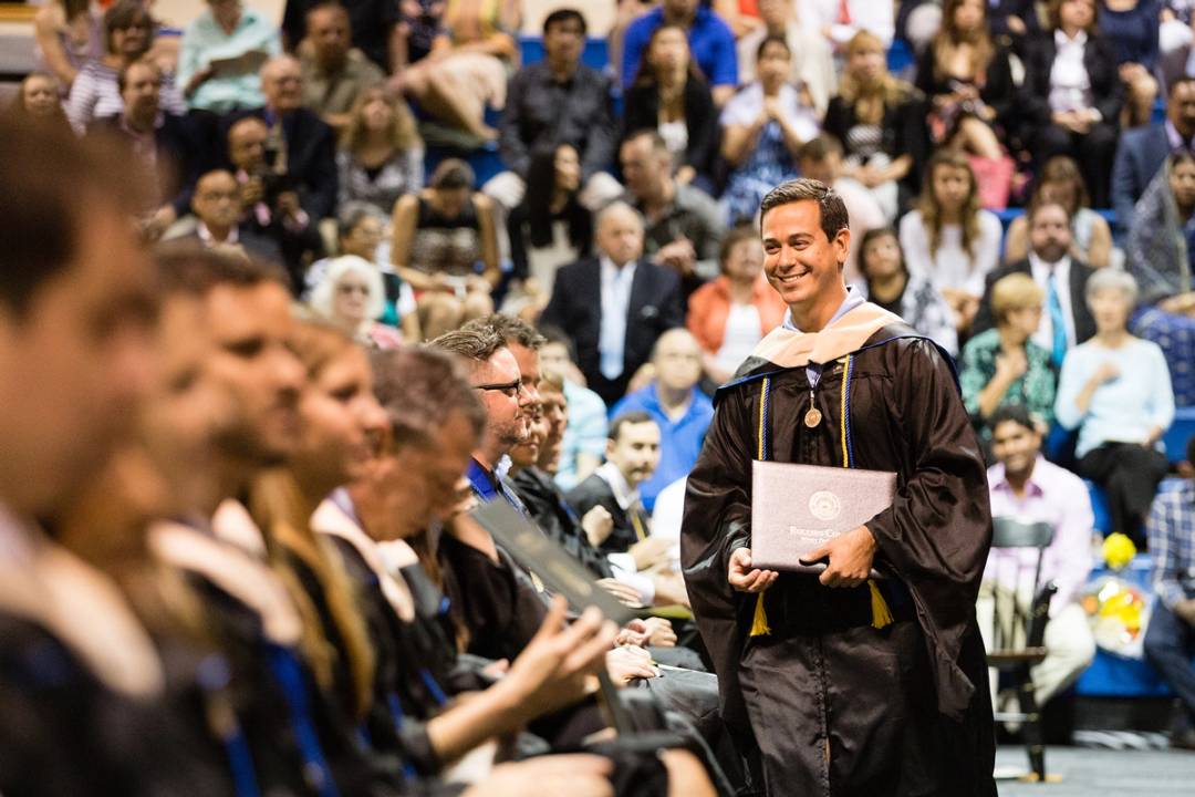 Student holding his diploma, walks back to his seat with a smile on his face, during the commencement ceremony