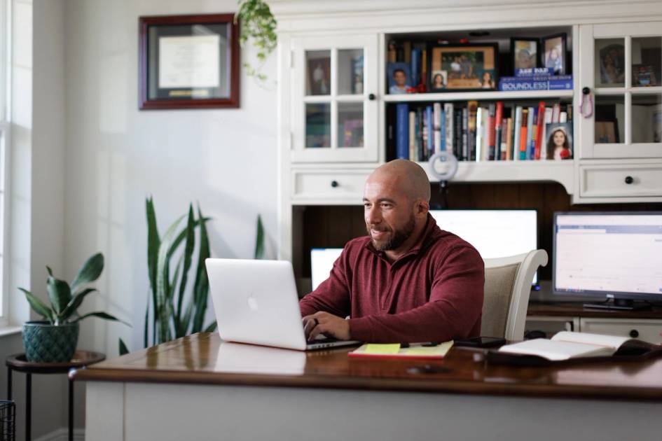 Man sitting at desk, typing on laptop.