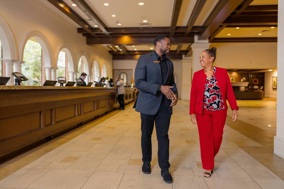 Hotel staff member walking with guest through spacious lobby near reception desk