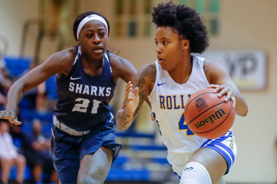 A women's basketball player dribbles past an opponent.