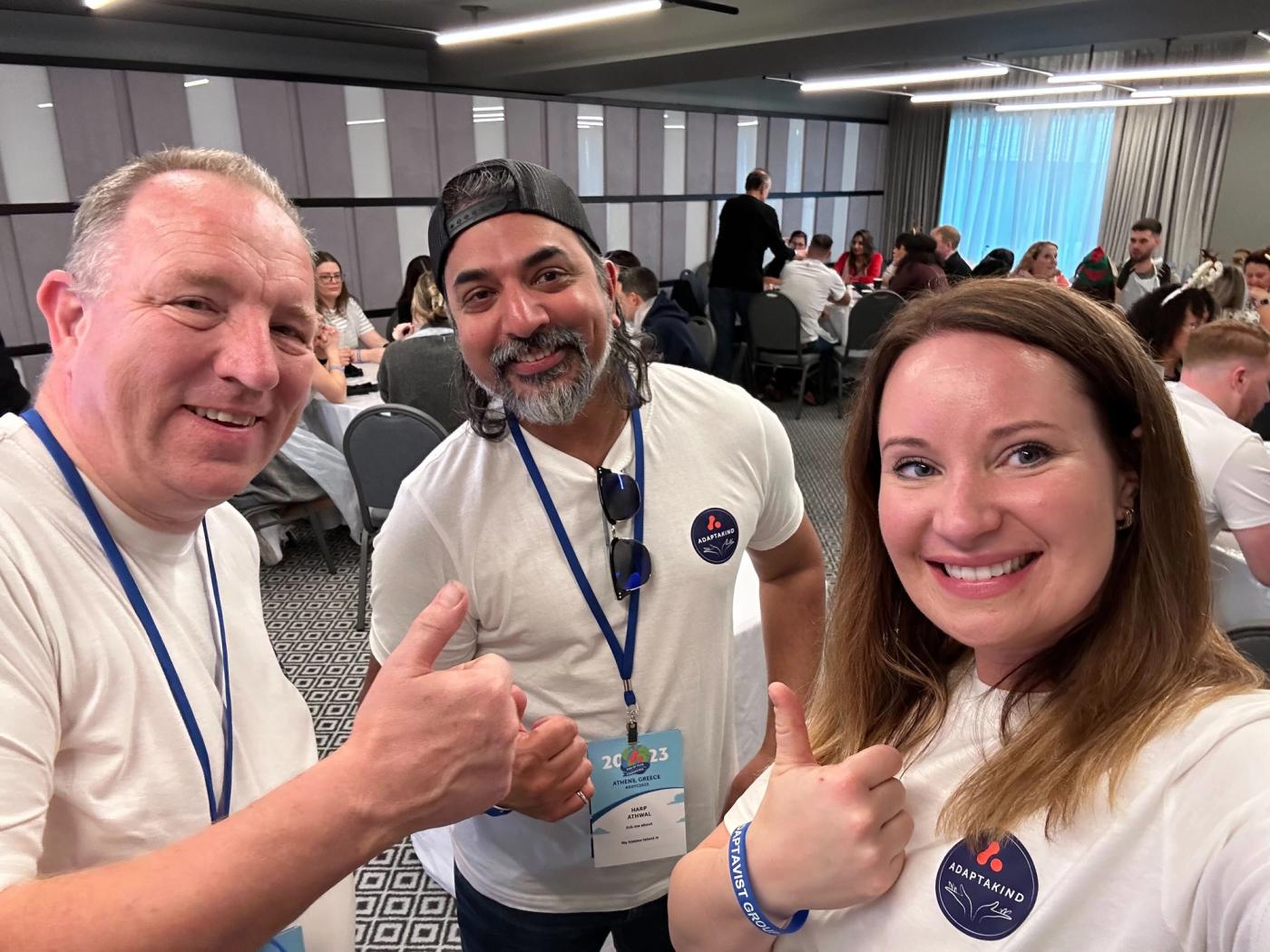 Phill Fox, Harp Athwal, and Ava Maitland at an event wearing AdaptaKind t-shirts. They are all smiling at the camera and giving a thumbs-up.