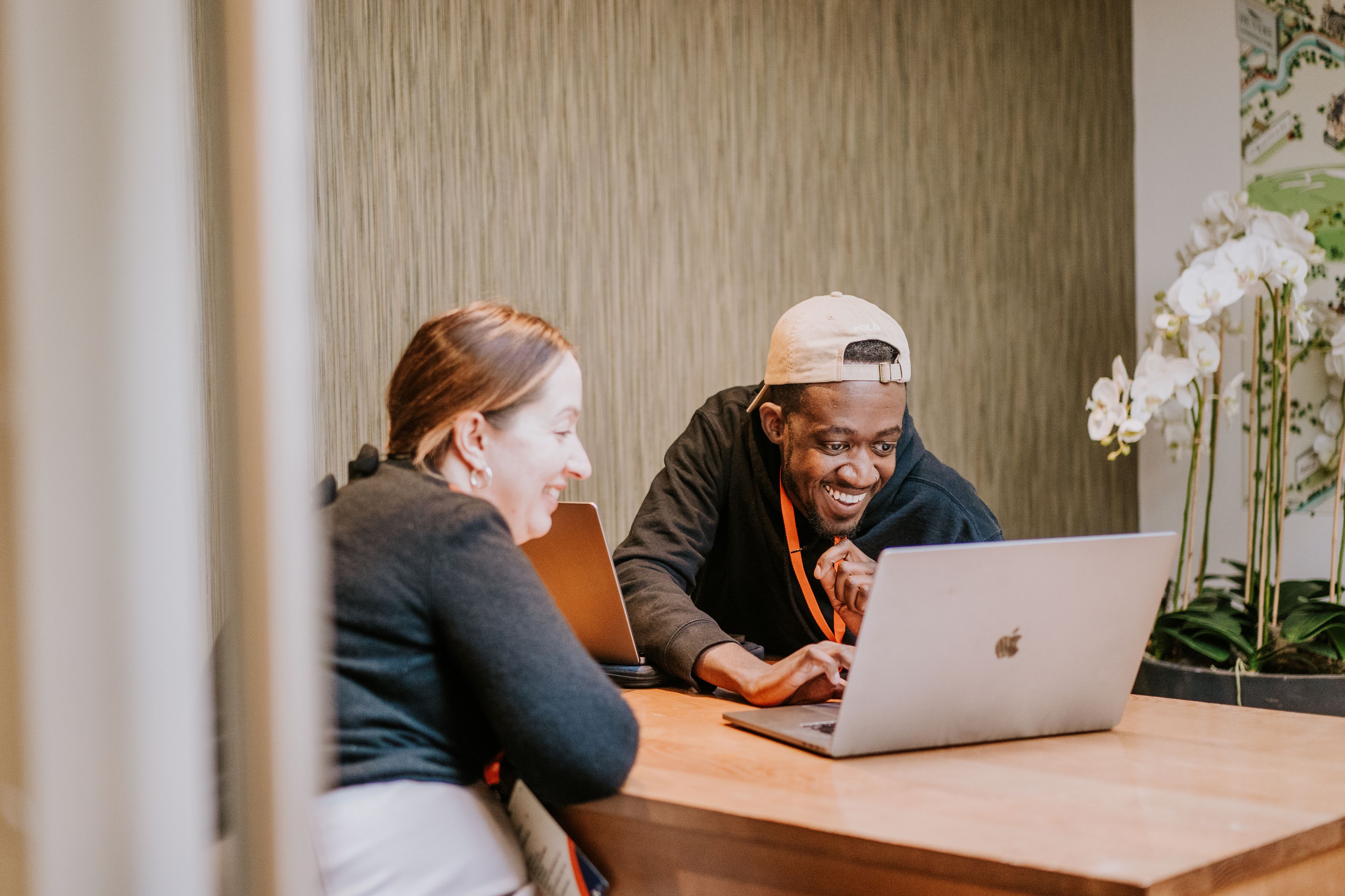Two people sitting at a table, looking at a laptop screen and smiling