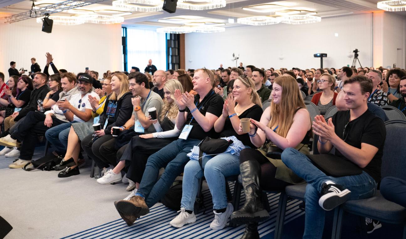 A large crowd seated in a conference hall, smiling and applauding