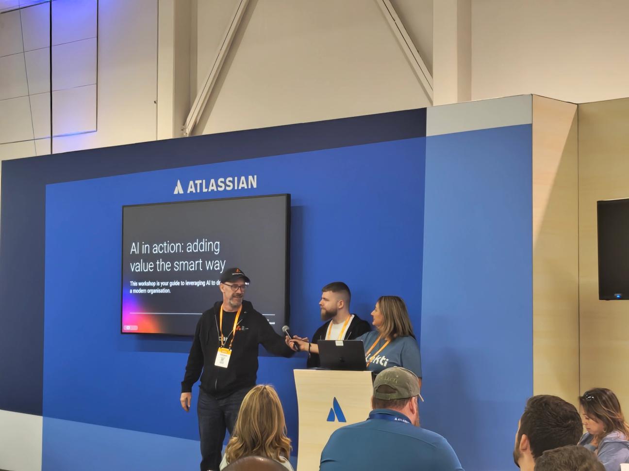 The Adaptavist Group colleagues at Atlassian Teams '25 event delivering a talk titled 'AI in action: adding value the smart way' as attendees watch.