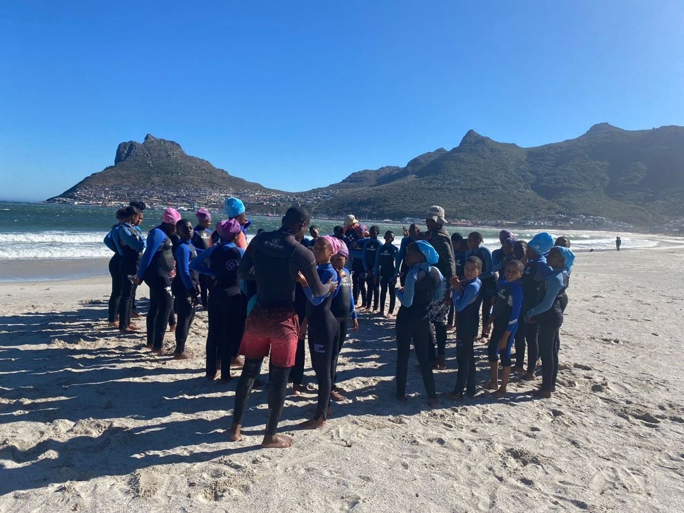 Volunteers standing on a sandy beach with mountains in the background, supervising a group of children