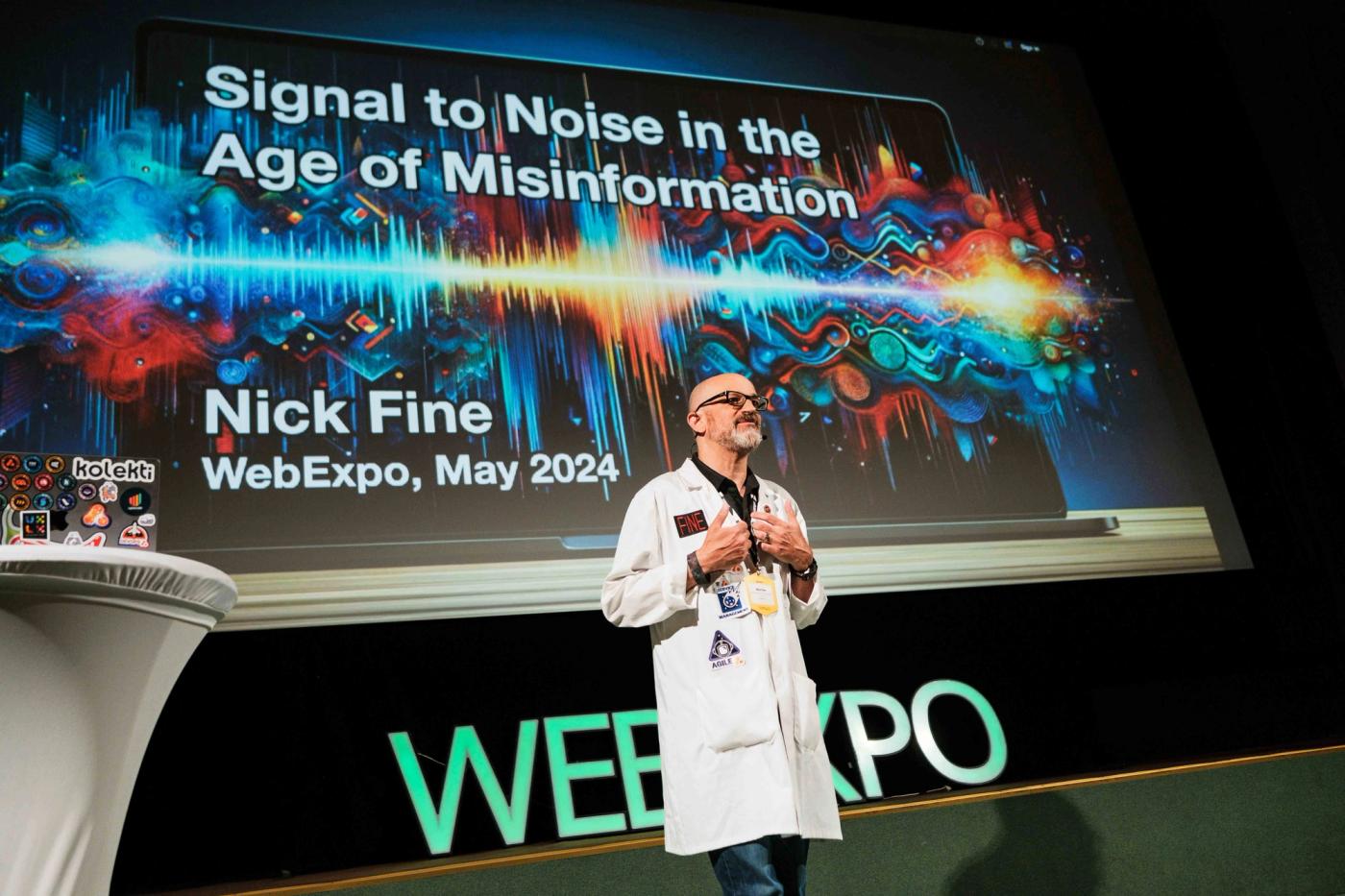 Dr Nick on stage in front of a large screen that reads 'Signal to noise in the age of misinformation'