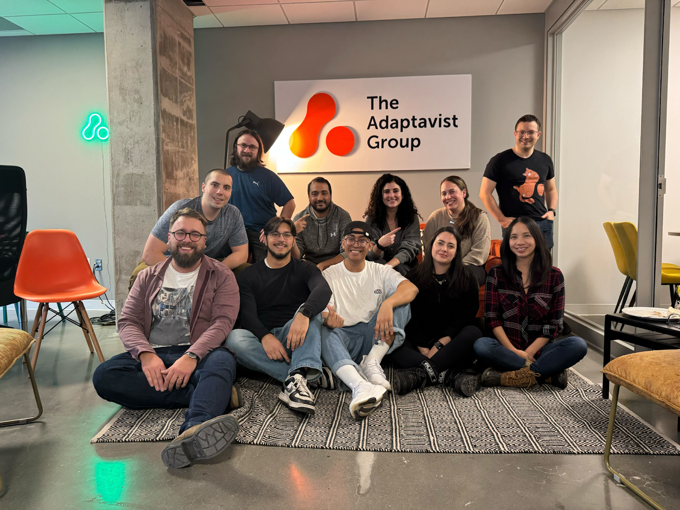 The Adaptavist Group volunteers sitting on the floor of a comfortable office space, in front of a sign with The Adaptavist Group's logo