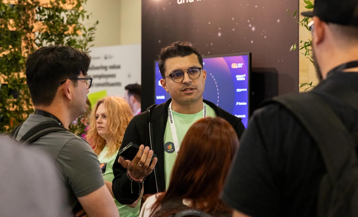 A person at The Adaptavist Group's event booth speaking to a group of customers