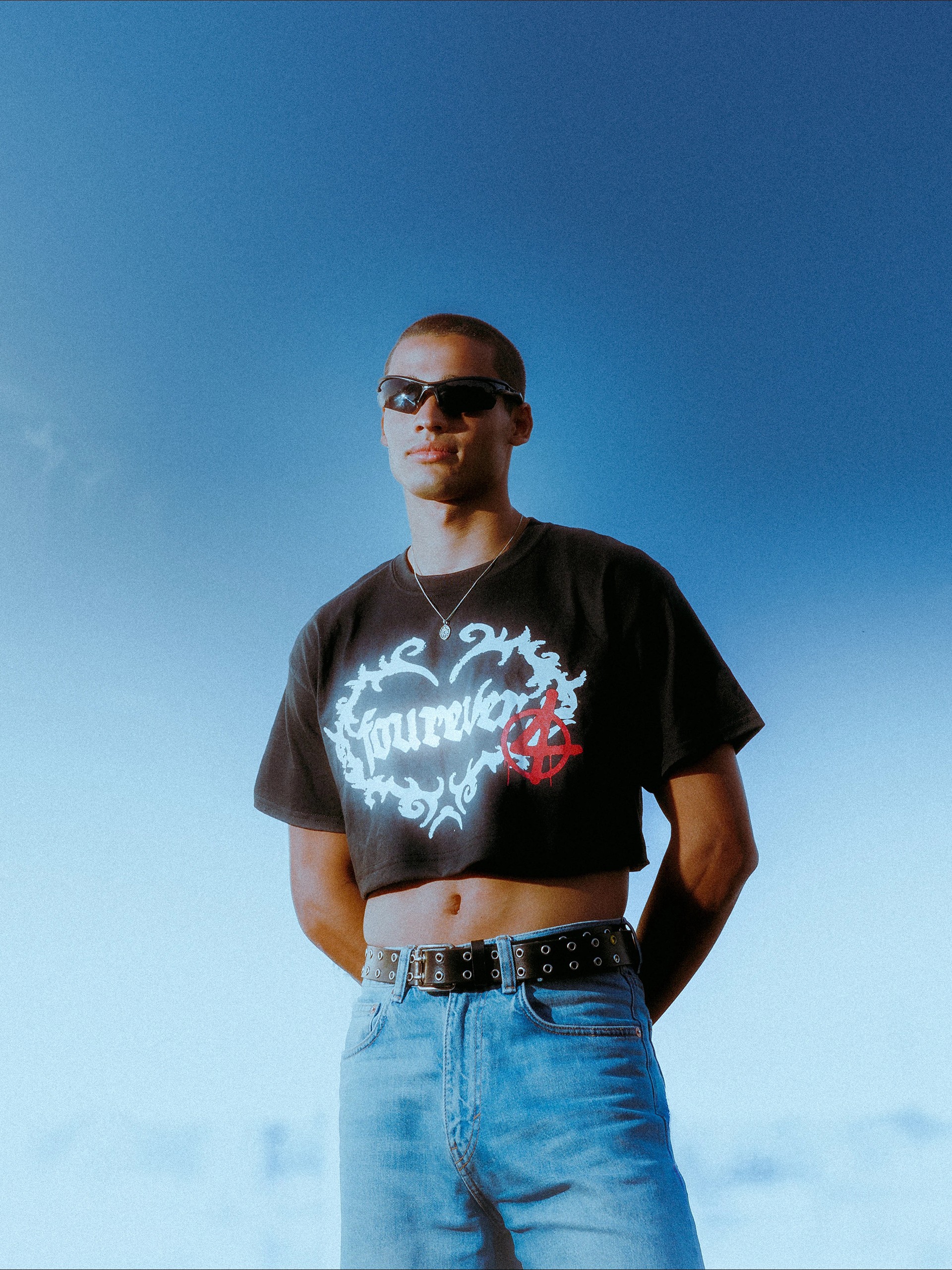 Model against a clear blue sky, white fourever graphic and red anarchy mark