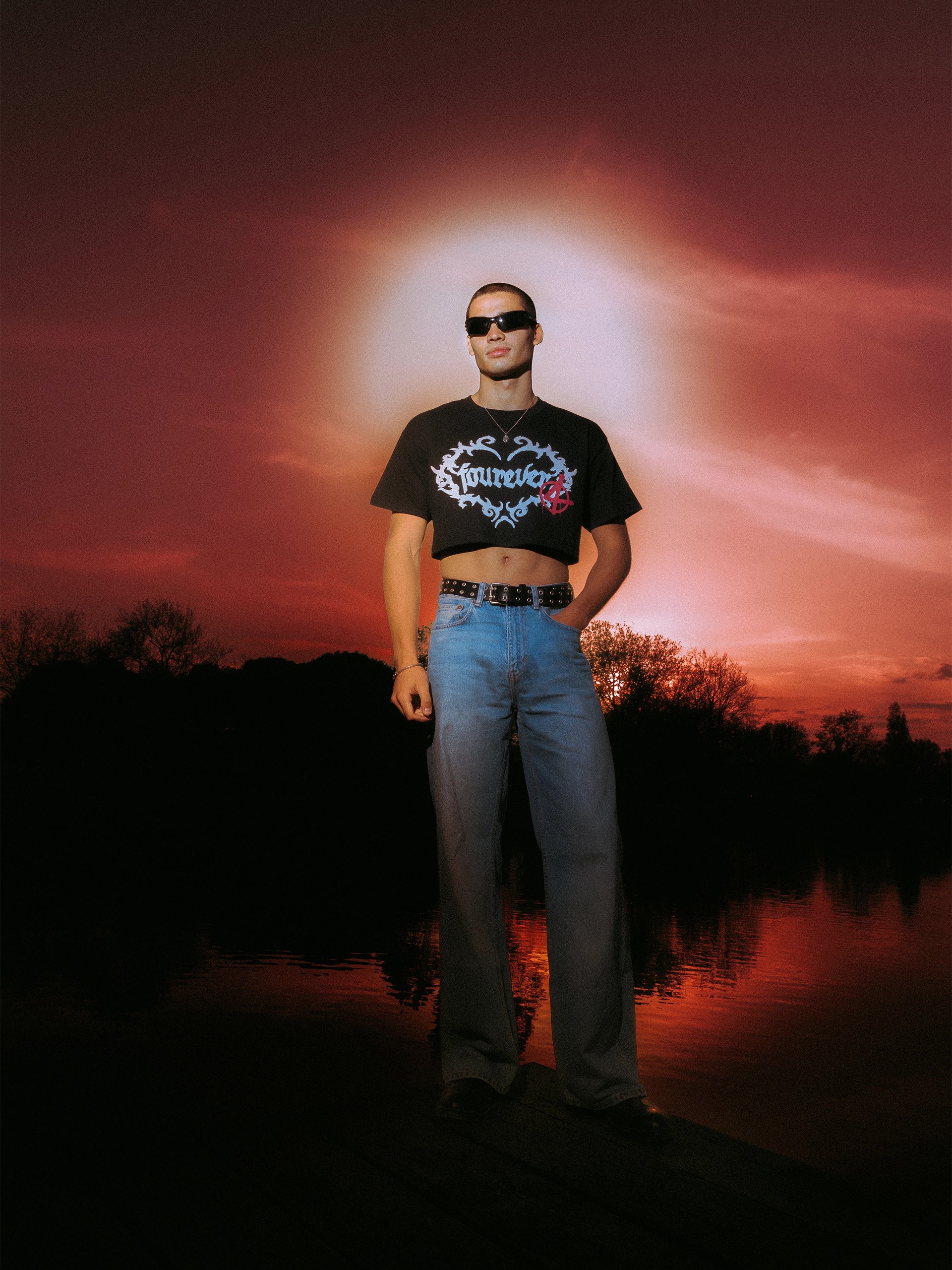 Model in the cropped fourever tee on a jetty, red sunset halo behind him