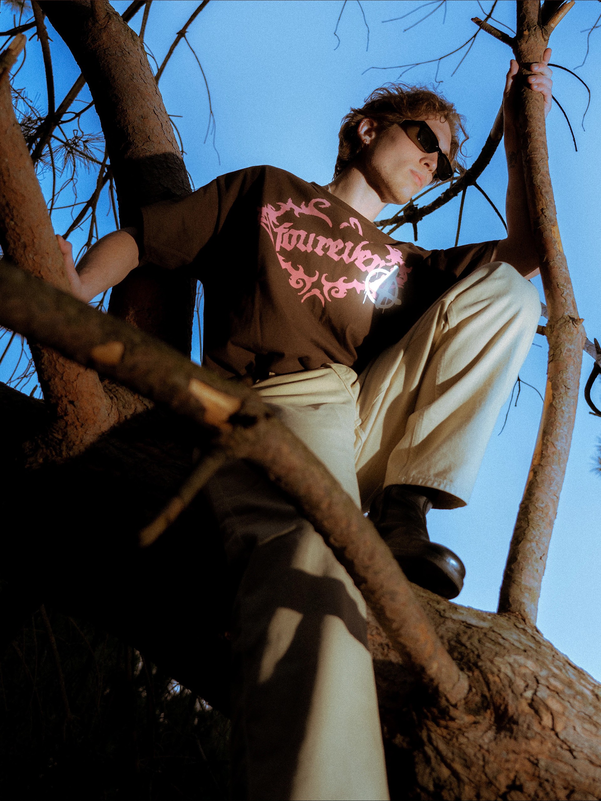Model lying back in the branches, pink fourever graphic on brown tee