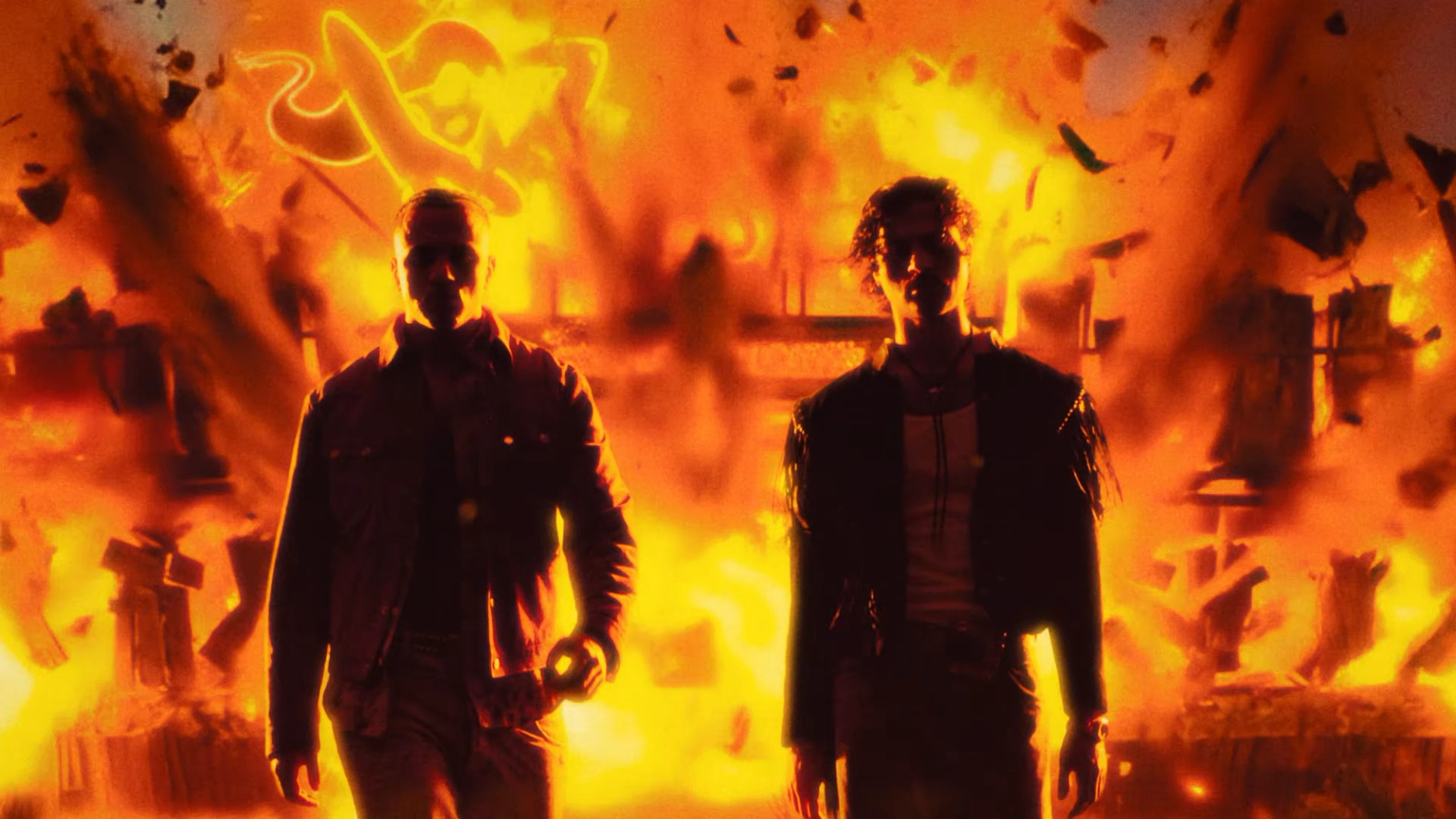 Two men walk toward the camera as a bar explodes behind them, silhouetted against bright orange flames and flying debris.