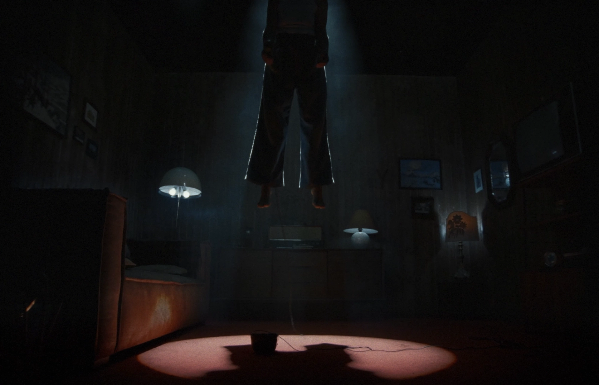 Elisa floats above the floor in a dark, wood-paneled room, illuminated by a beam of light.