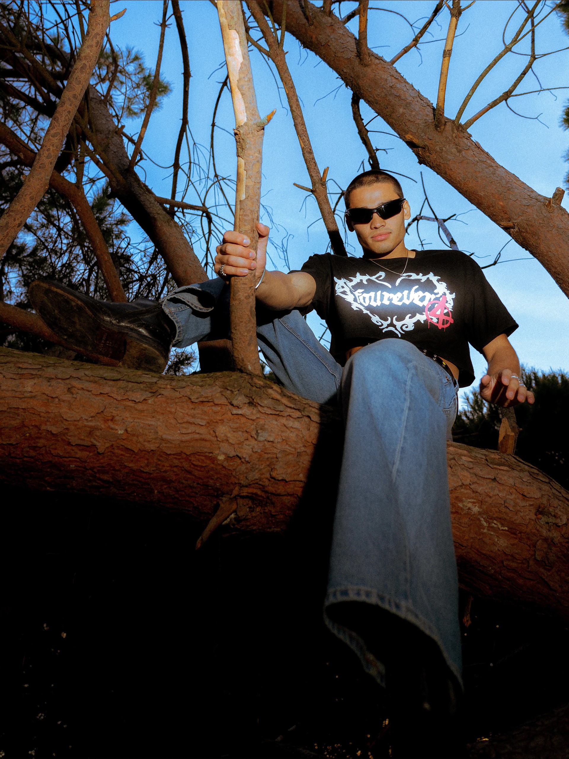 Model seated on a fallen pine trunk, holding a branch