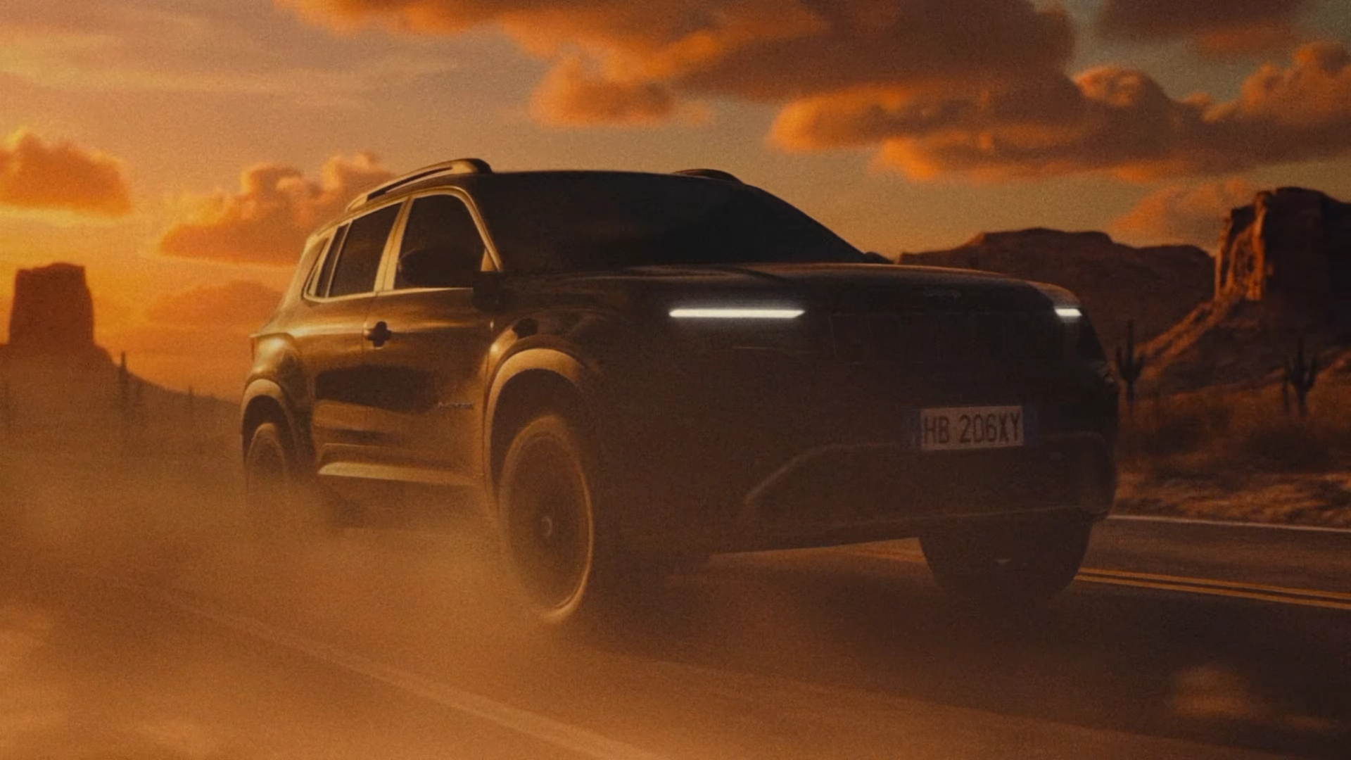 Low-angle view of a dark SUV driving through dust on a desert road, with rocky mesas beneath an orange sunset sky.