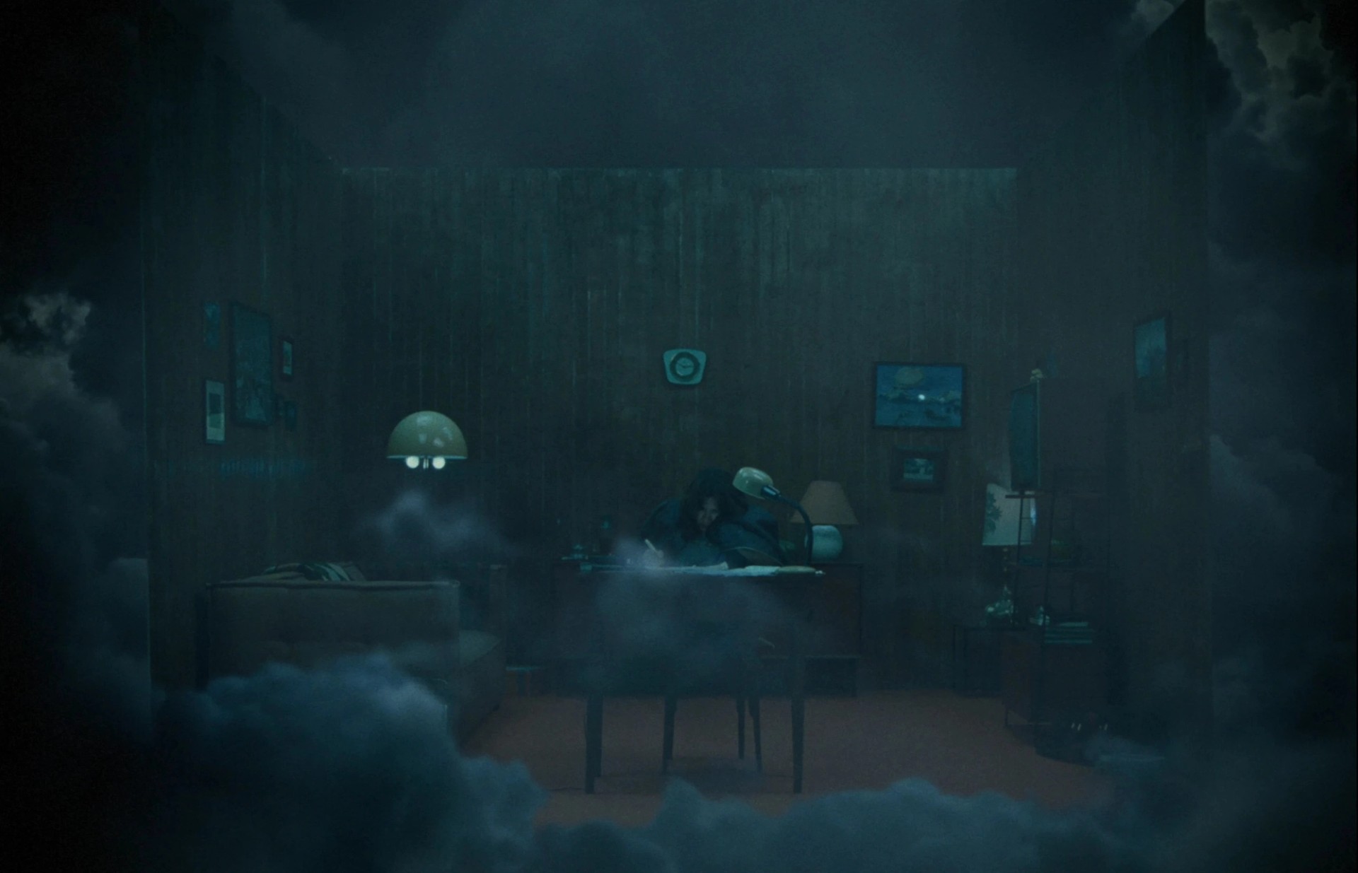 A woman writes at a desk in a dim, wood-paneled room surrounded by dark clouds and blue mist.