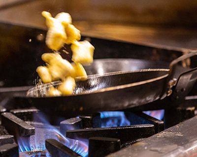 A pan with food being flipped in the air over a commercial gas stove