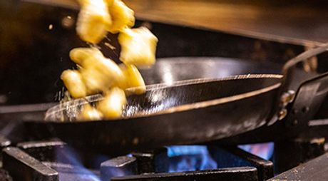 A pan with food being flipped in the air over a commercial gas stove