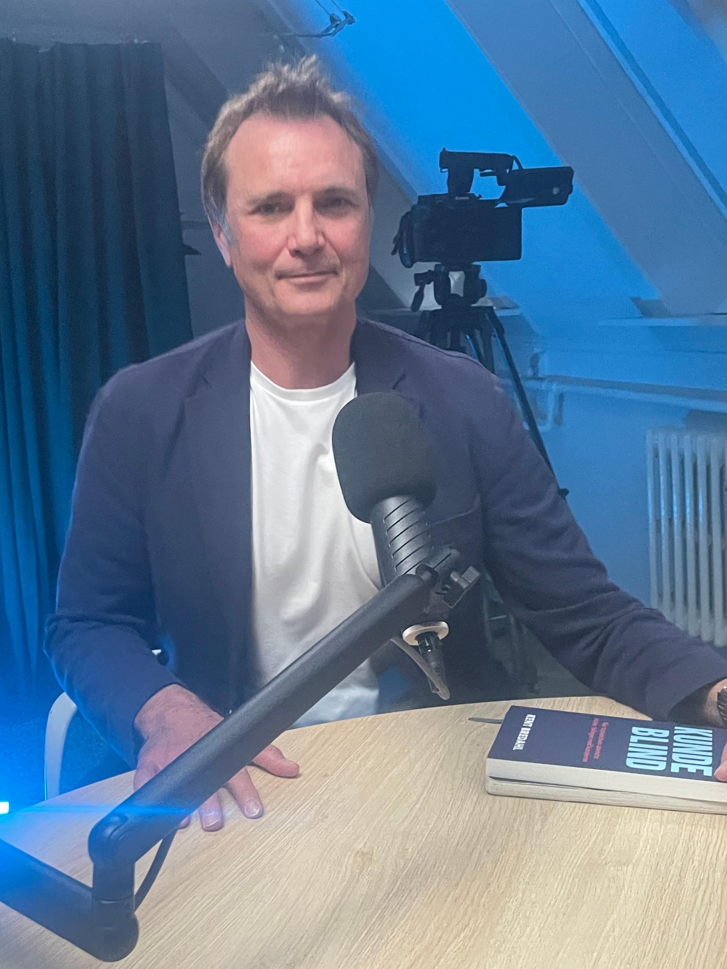 Kent Bredahl ved mikrofonen i NexusOnes podcaststudie med sin bog Kundeblind på bordet under optagelsen af afsnit 4