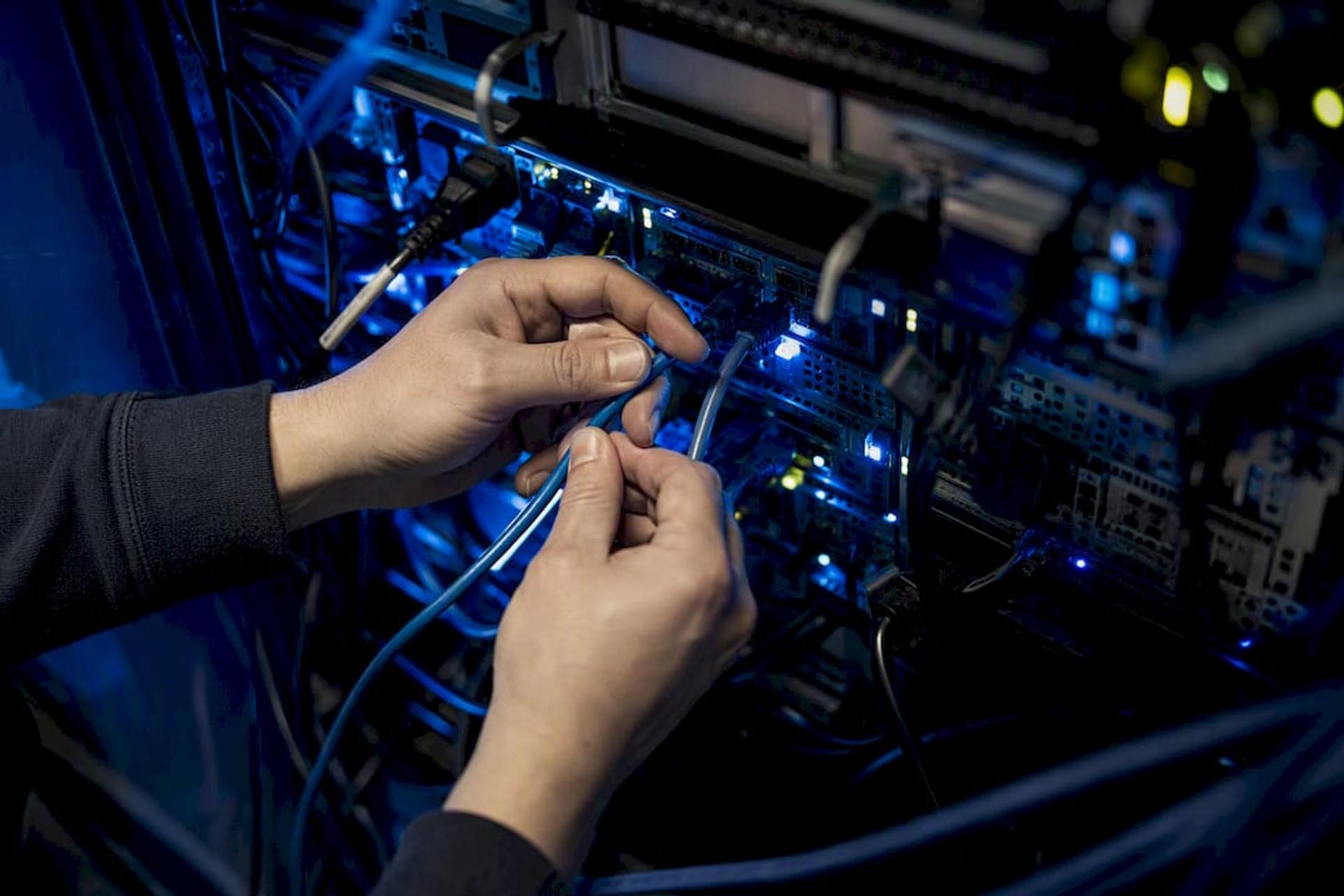 Hands connecting network cable to server rack