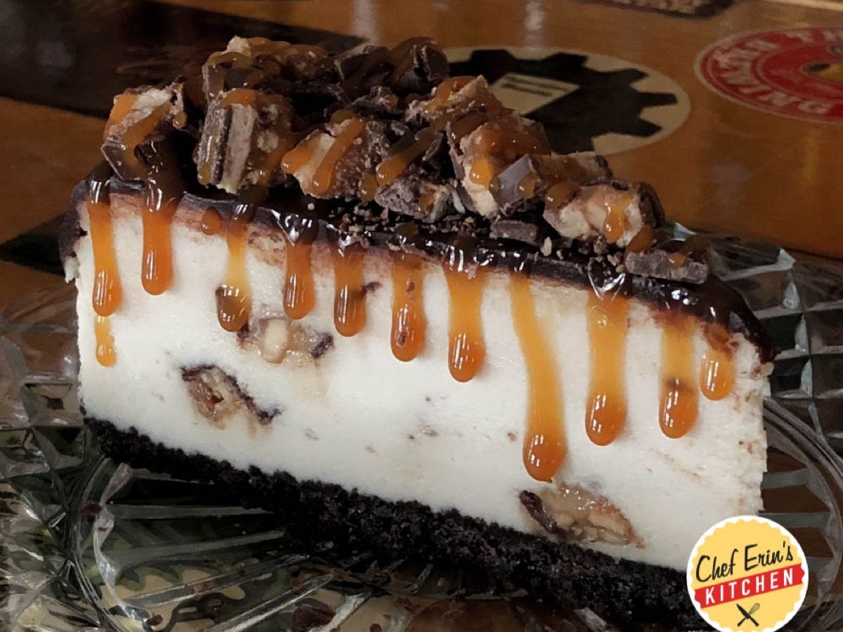 A slice of Snickers cheesecake drizzled with caramel and topped with candy bar chunks
