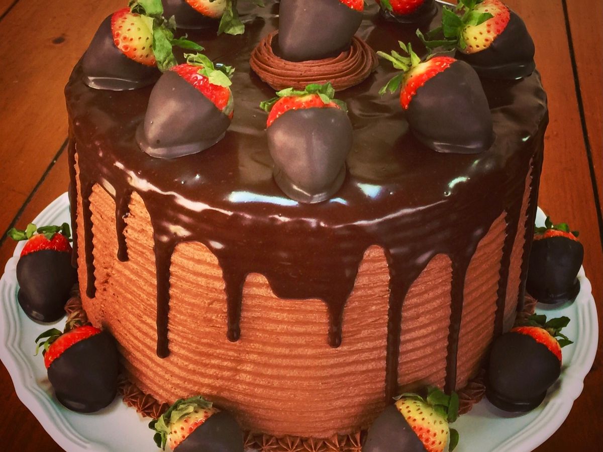 A tall layer cake alternating chocolate and strawberry cake, topped with chocolate covered strawberries