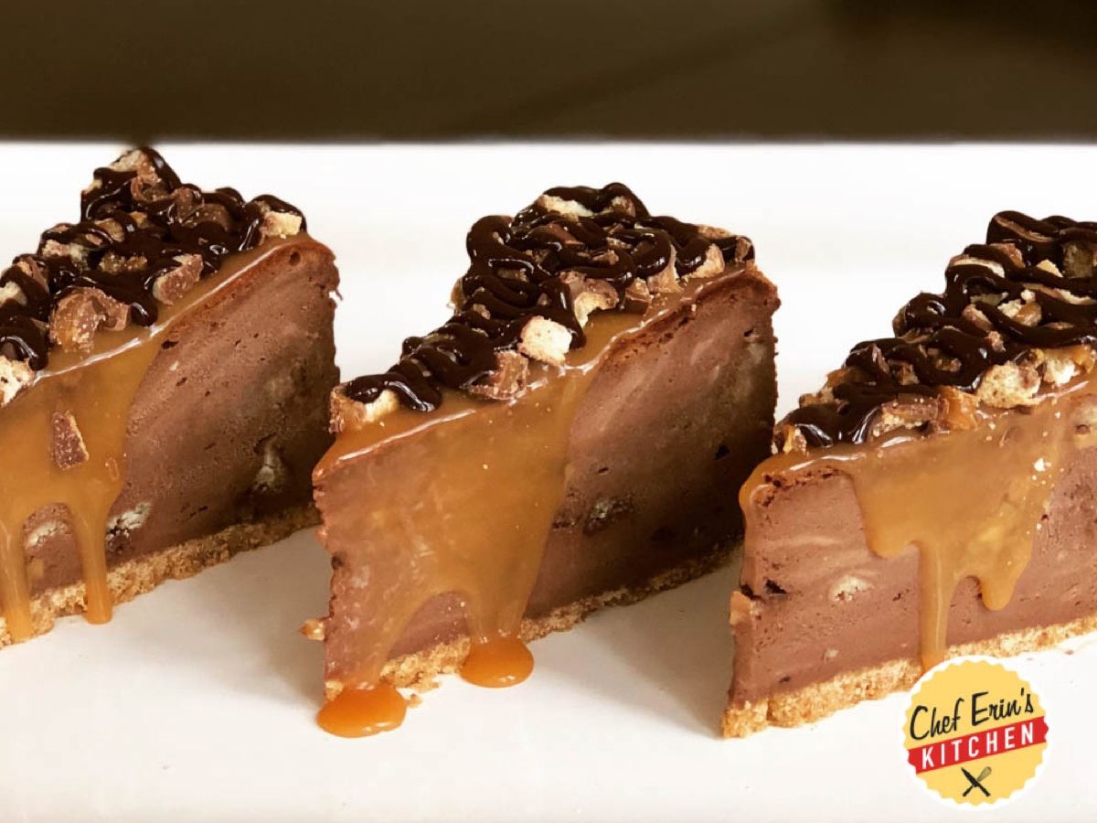 A slice of chocolate cheesecake topped with caramel, chocolate ganache, and Twix candy bar pieces