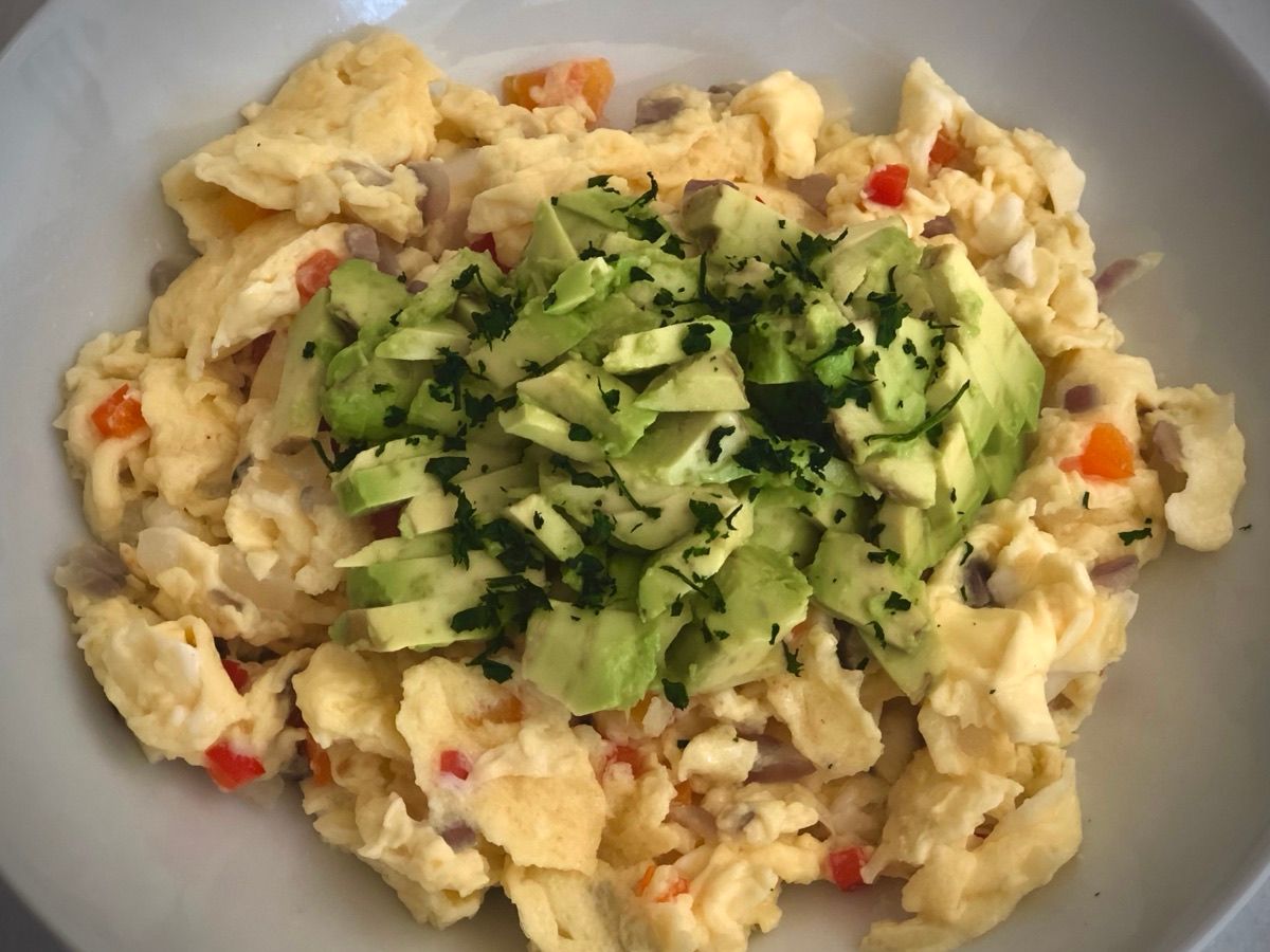 A plate of scrambled eggs topped with sliced avocado