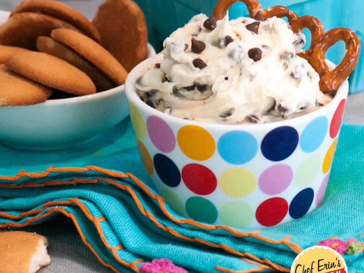 A bowl of cookie dough dip surrounded by graham crackers and pretzels