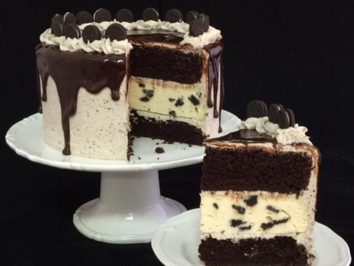 A layered chocolate cake and Oreo cheesecake dessert covered in ganache and mini Oreos